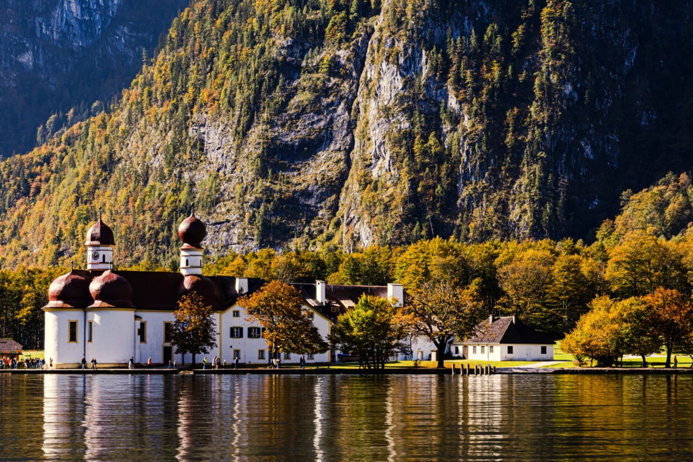 St. Bartholomä Malerei der Kirche mit Zwillingskuppeln am Ufer eines Sees, umgeben von Bergen und Bäumen.