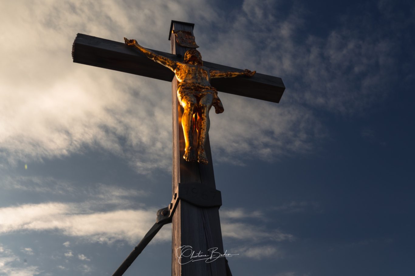Auf dem Predigtstuhl Goldener Christus am Holzkreuz vor Wolkenhimmel.